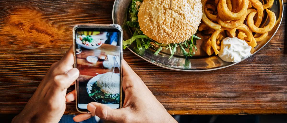 close up of a restaurant patron using a smart phone and snapping a picture of their meal